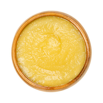 Apple sauce in a wooden bowl. Commercially processed applesauce, a yellow sauce made of peeled and cooked apples. Inexpensive and widely consumed in North America and parts of Europe. Macro food photo