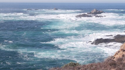 Rocky craggy ocean beach. Big waves crashing on bare cliff, blue water splashing, sea foam. Power of nature near Big Sur, 17-mile drive. Dramatic seascape. Point Lobos, Monterey, California coast, USA