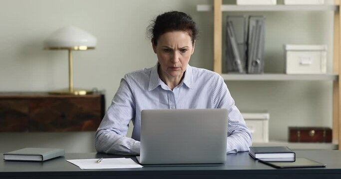Irritated old age lady employee look on laptop screen shocked with broken app spam computer virus attack. Outraged annoyed mature woman office worker deal with problem incorrect software work using pc