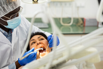 Dentist in face mask inspects female patient teeth with mirror and probe