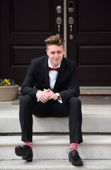 Young man in formal suit and bow tie sitting on front steps of house