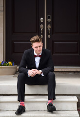 Young man in formal suit and bow tie sitting on front steps of house