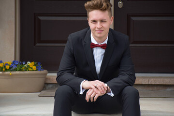 Young man in formal suit and bow tie sitting on steps at front door of house © Julia