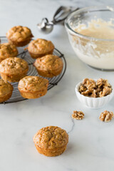A cooling rack of carrot cake muffins with a bowl of cream cheese icing.