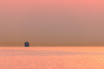 Single container ship on horizon with red hazy glow