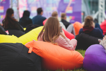 Audience at the open air venue listens to lecturer, people on a bean bags together listen to speaker on stage at master-class, corporate business seminar outdoors