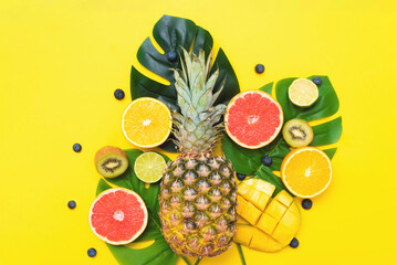Summer poster. Summer juicy fruits and berries on monstera palm leaves on a yellow background.