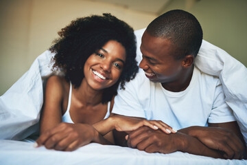 Its hard not to be happy waking up to love. Portrait of a happy young couple relaxing under a duvet...