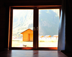 View from inside the room overlooking a clearing and a small house in the mountains in the early morning.