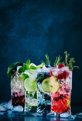 Fototapeta na wymiar Cold summer cocktails drinks. Classic alcoholic long drink and mojito or mocktail in highballs with blueberries, blackberries, raspberries, lime, herbs and ice on blue background