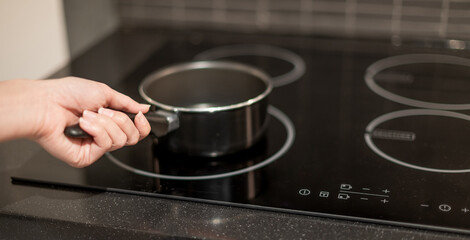 Female hand holding a pot that is put on the electric pan in the kitchen.