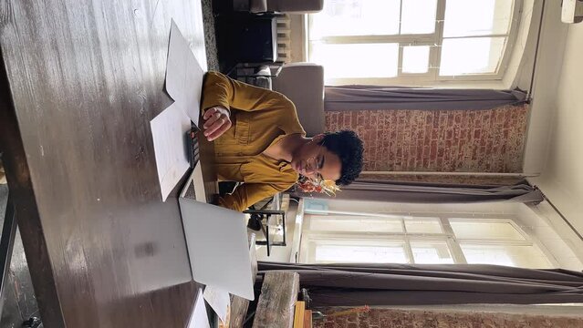 Serious young Black businesswoman do budgeting paperwork at home office calculate bills to pay online via laptop review financial papers check sums in invoices notifications. Vertically oriented video
