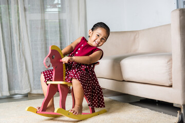 Asian cute little girl swinging riding toy horse, Smiling kid playing horse rocking chair at home...