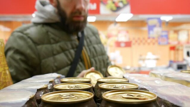 Close-up of many cans of beer on a store shelf and a man takes a few cans