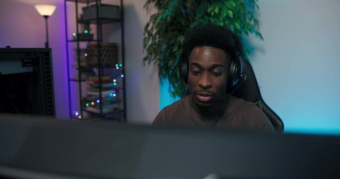 A player is playing on a computer with his team, with whom he is talking through a headset; a man clicks on a keyboard with one hand, tweaks a microphone with the other.
