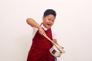 Angry asian boy with apron standing while holding a kitchen ware. Cooking class concept