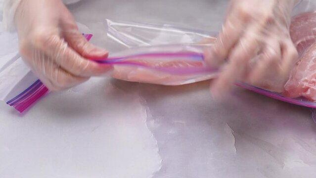Fresh raw fish fillet in zip lock bags. Tilapia fillet on light marble background, close up. Woman hands put  fillet in zip lock bags for freezing