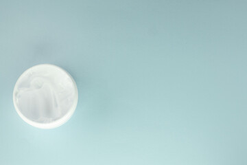 White cosmetic face cream in a round open jar on a light blue background, top view, copy of the space on the right