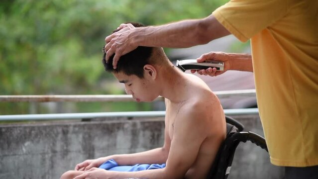 Young man with a disability on wheelchair giving dad a haircut, He had a tremor caused by Cerebral palsy has symptoms similar to Parkinson's disease,Health care for people with disabilities concept.