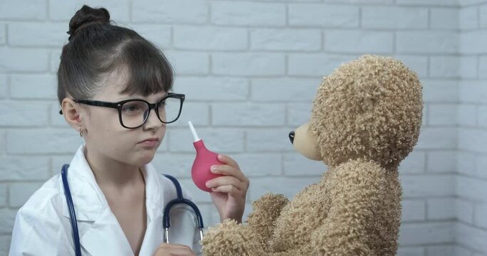 Play doctor with toy. A little girl play with her teddy bear like a doctor with an enema in her hand.