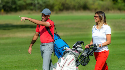 Young couple enjoying a game of golf, walking the fairway on a golf course on a beautiful sunny day