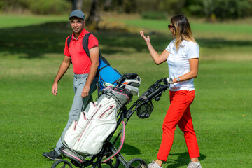 Obraz premium Young couple enjoying a game of golf, walking the fairway on a golf course on a beautiful sunny day