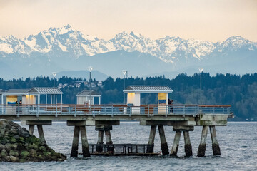 Complex clouds and stark mountains overshadow a fishing pier on Puget Sound