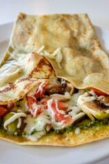 A vegetable crepe with cheese, mushroom, tomato and pesto on a plate