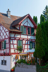 Historic tenement house with white walls, red half timbered elements and dark green shutters on a old town street in a Swiss touristic city 
