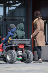 Obraz na płótnie Canvas Mom is standing near a toy ATV with two sons on a spring day