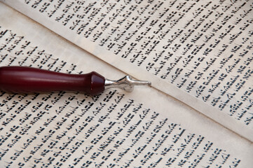 Fototapeta premium Reading the Torah, the five holy books of Moses and Judaism with the assistance of a pointer or yad to guide the reader through the Hebrew text.