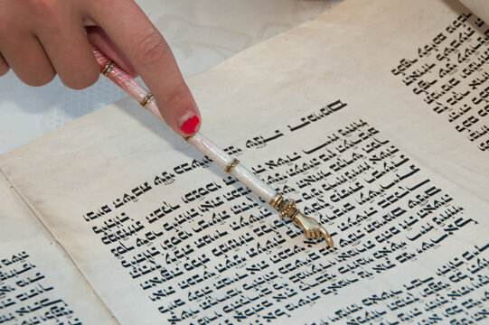 Reading the Torah, the five holy books of Moses and Judaism with the assistance of a pointer or yad to guide the reader through the Hebrew text.