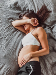Tired pregnant woman sleeping on bed hiding face crying in depression or feeling morning sickness nausea. Mental health, fatigue, stress during pregnacy
