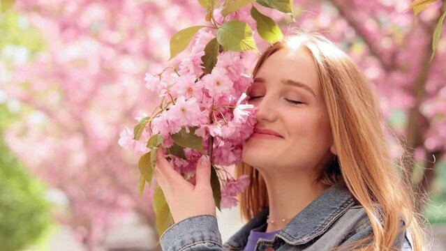 Close up portrait young face woman with beautiful eyes looking and smiling at the camera on blurred background in the city street. Sacura tree. Happy Caucasian girl with Cherry blossom trees.