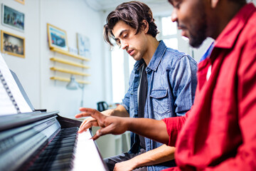 latin hispanic man learning to play on piano with caucasian teacher in classroom