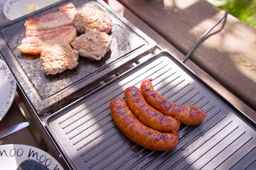 Bacon and sausages on an electric grill in the garden