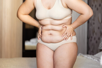 Fototapeta na wymiar Cropped of overweight fat woman holding tummy flabs with obesity, excess fat in underwear. Inclination body. Adipose stomach. Big size. Go on unhealthy diet. Emphasizing excess adiposity. Excess skin
