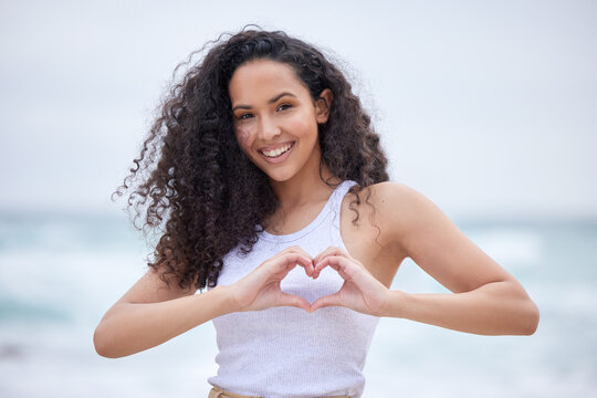 Love yourself before anything else. Shot of a young woman making a heart gesture with her hands at the beach.