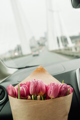 chic large bouquet of pink tulips in kraft packaging in the car interior on the background of the road. flower content, flower delivery, selective focus