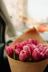 chic large bouquet of pink tulips in kraft packaging in the car interior on the background of the road. flower content, flower delivery, selective focus