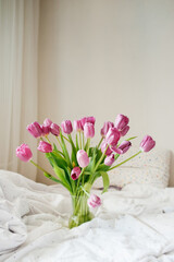 beautiful large bouquet of pink fresh tulips in vase on white linen bed in natural beautiful light. good morning mood. holiday card. cover for printing. selective focus