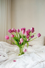 beautiful large bouquet of pink fresh tulips in vase on white linen bed in natural beautiful light. good morning mood. holiday card. cover for printing. selective focus