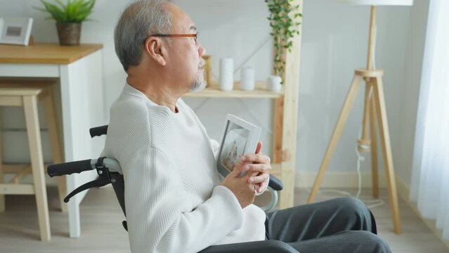 Asian senior male sit alone on wheelchair and looks family photographs