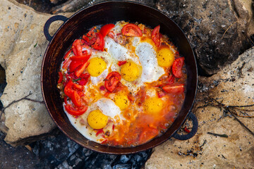 Eggs prepared with vegetables on a frying pan on the fire in the forest. Cooking scrambled eggs over an open fire. Breakfast in nature. Tourist food.