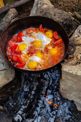 Eggs prepared with vegetables on a frying pan on the fire in the forest. Cooking scrambled eggs over an open fire. Breakfast in nature. Tourist food.