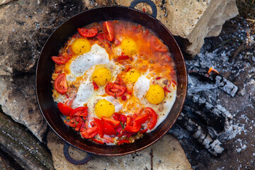 Fototapeta na wymiar Eggs prepared with vegetables on a frying pan on the fire in the forest. Cooking scrambled eggs over an open fire. Breakfast in nature. Tourist food.
