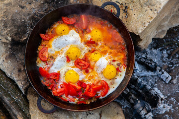 Eggs prepared with vegetables on a frying pan on the fire in the forest. Cooking scrambled eggs over an open fire. Breakfast in nature. Tourist food.