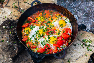 Eggs prepared with vegetables on a frying pan on the fire in the forest. Cooking scrambled eggs over an open fire. Breakfast in nature. Tourist food.