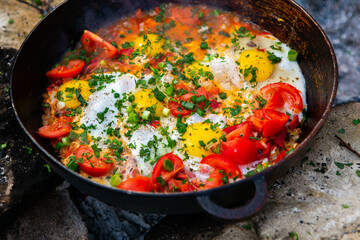 Eggs prepared with vegetables on a frying pan on the fire in the forest. Cooking scrambled eggs over an open fire. Breakfast in nature. Tourist food.