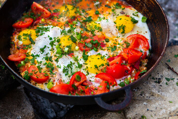 Eggs prepared with vegetables on a frying pan on the fire in the forest. Cooking scrambled eggs over an open fire. Breakfast in nature. Tourist food.
